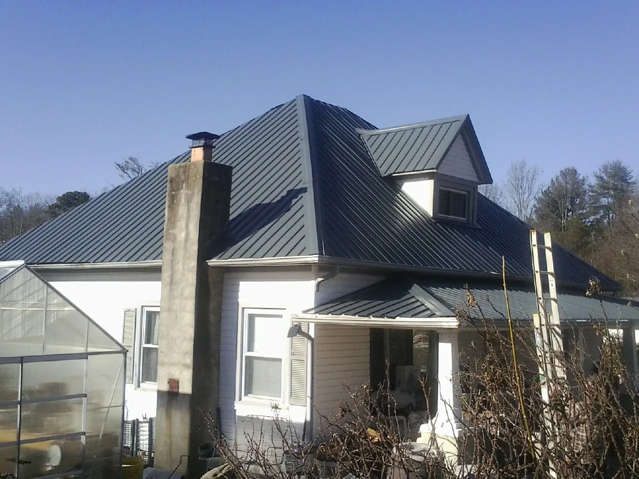 Dark blue standing seam metal roof on a white farmhouse with dormer — Slate & Tile Roof Repair by Roofing Brothers in Collegeport