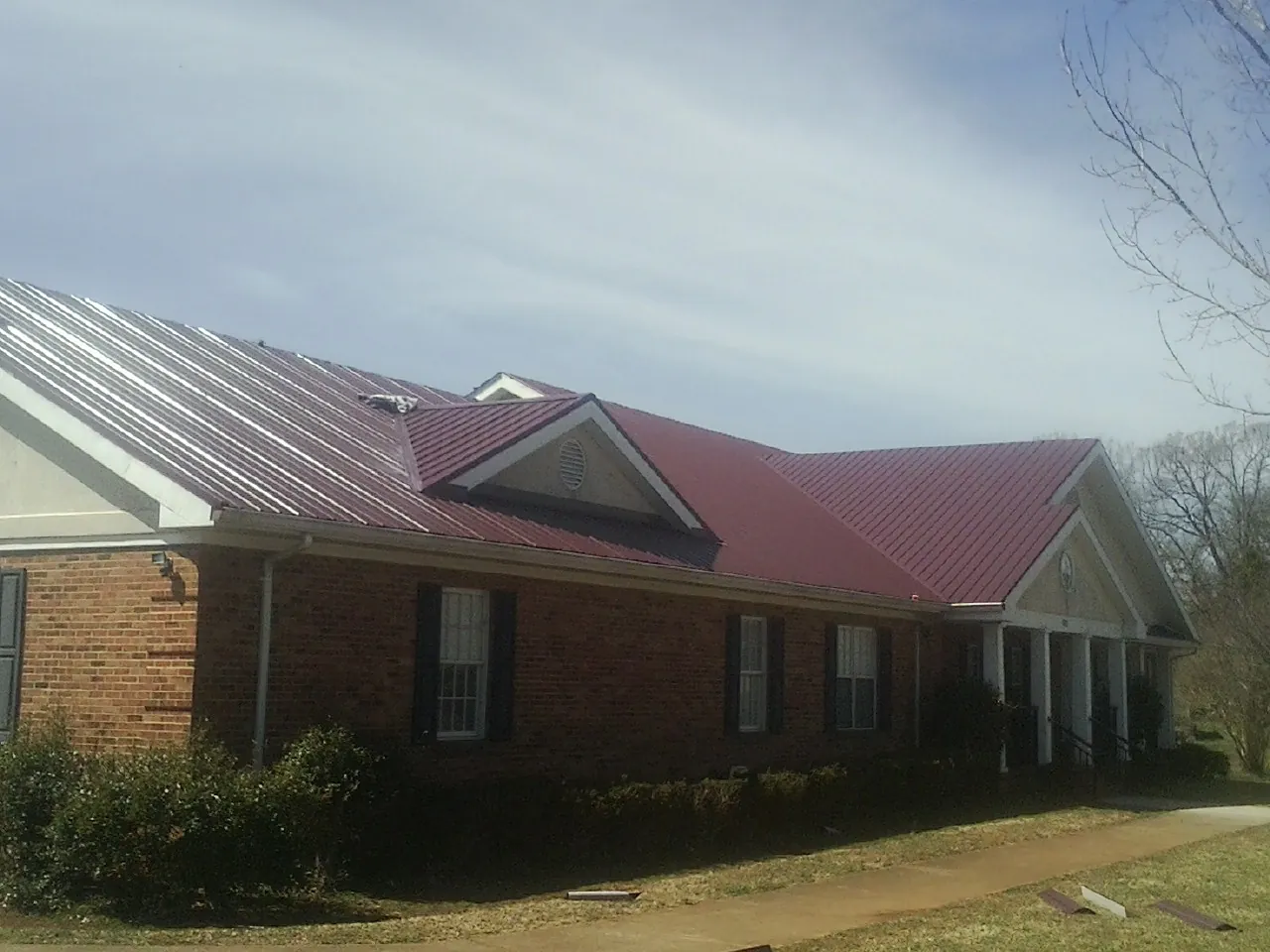 Red metal roof with gabled entries on a long brick building, from a Hail Damage Roof Repair job in Collegeport