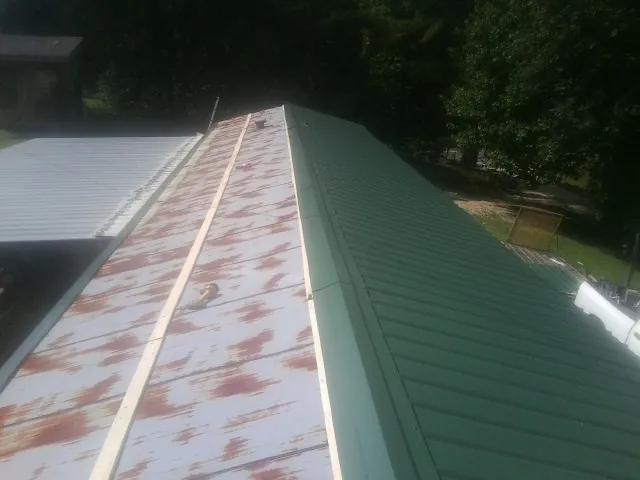 Old rusted panels beside newly installed green metal roofing — Wind Damage Roof Repair by Roofing Brothers in Collegeport