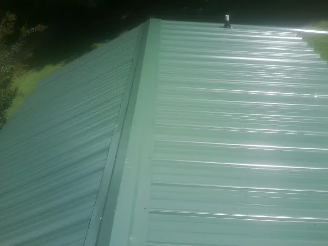 New green metal panels meeting at the ridge of a roof — Flat Roof Repair work by our crew in Collegeport