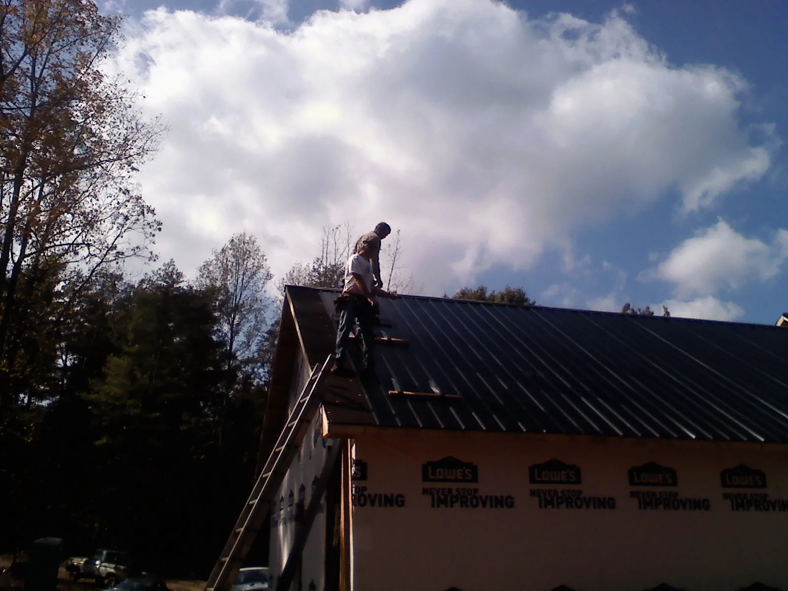 Roofer fastening dark metal panels high against a cloudy sky, from a Roof Inspection job in Collegeport