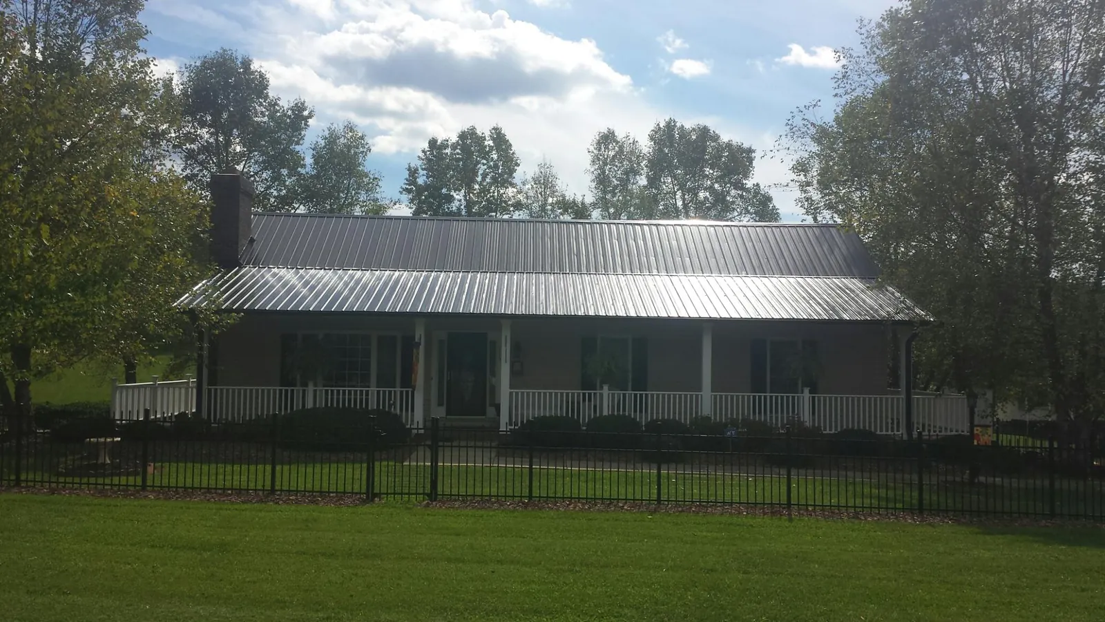 Gray metal roof on a brick ranch with a full width front porch — Gutter Guard Installation work by our crew in Collegeport