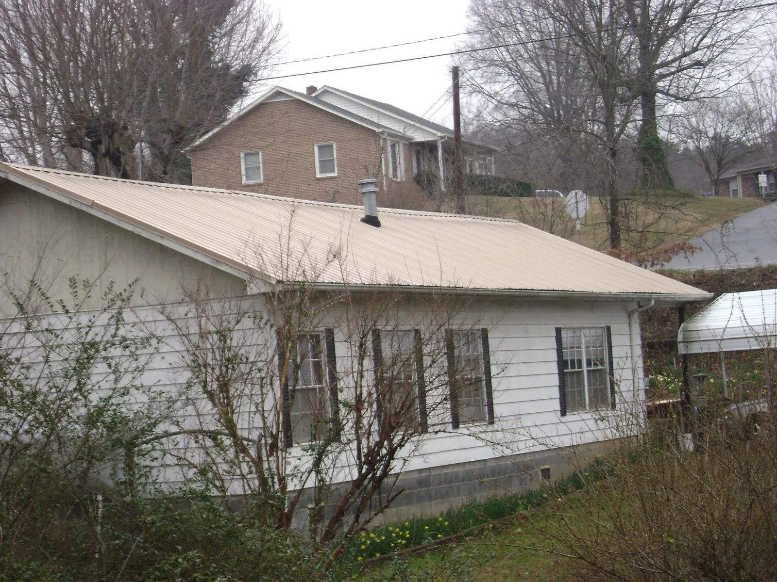 Tan metal roof on a white sided house set into a hillside — Commercial Roofing by Roofing Brothers in Collegeport