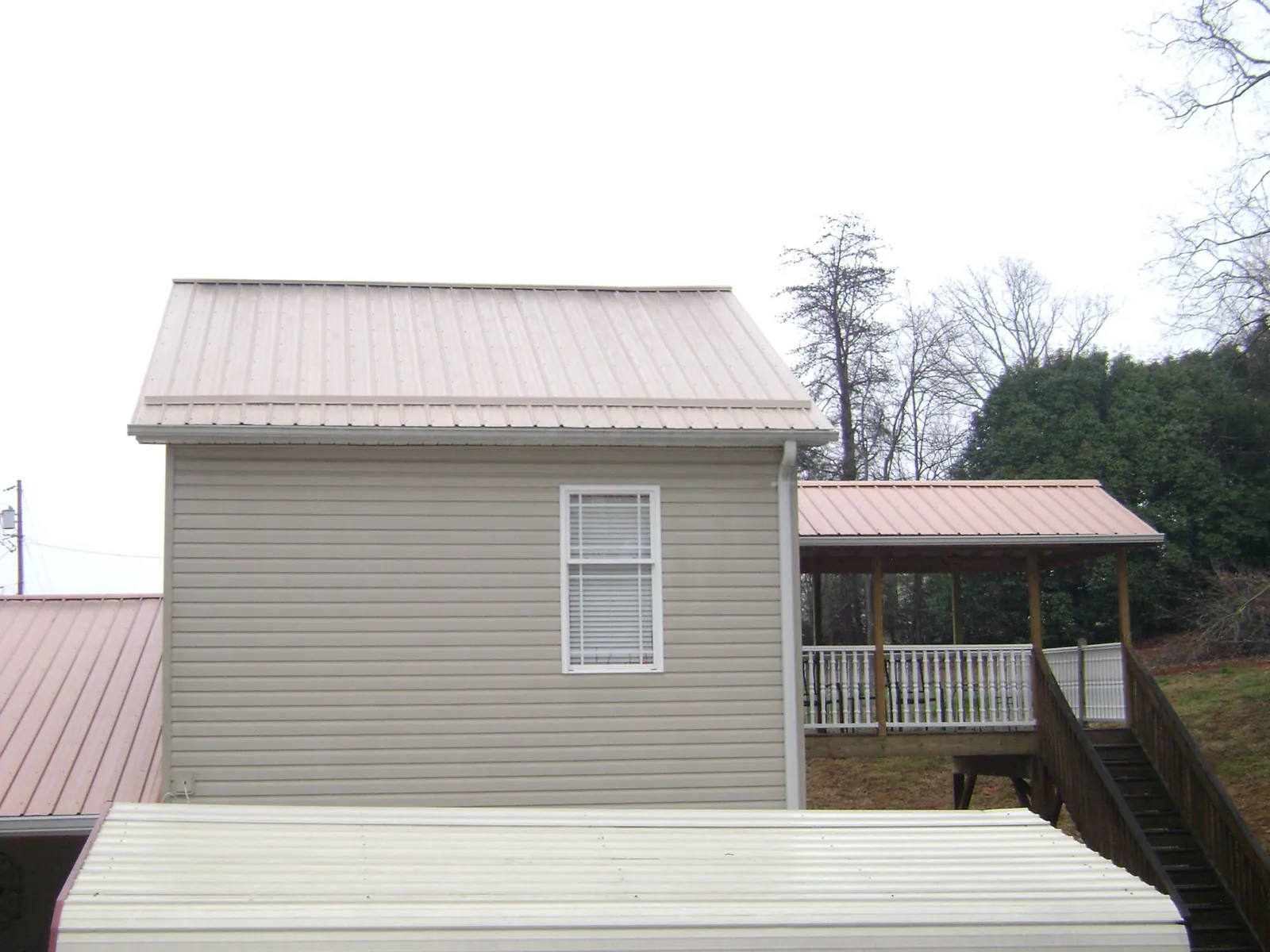 Tan metal roofs on a two story addition and attached porch, from a Roof Replacement job in Collegeport